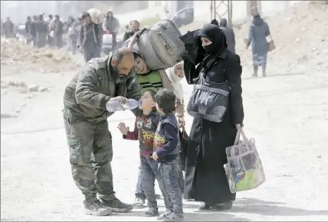  ?? Louai Beshara/AFP/Getty Images ?? A member of the Syrian government forces helps children drink from a water bottle during a civilian evacuation Thursday from the eastern Ghouta enclave on the outskirts of the capital Damascus.