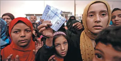  ?? ZOHRA BENSEMRA / REUTERS ?? A woman shows her refugee identifica­tion paper as she complains about the lack of food supplies outside a processing center as smoke from a burning oil refinery blanketed Qayyara, south of Mosul, Iraq, on Sunday.