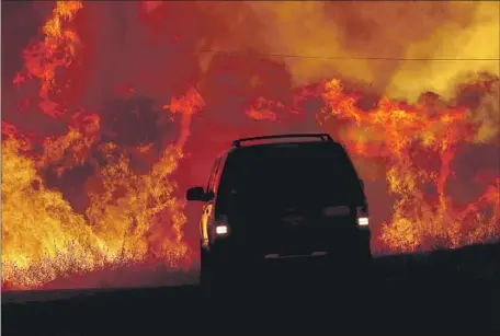  ?? Luis Sinco Los Angeles Times ?? A MOTORIST drives past flames from the Fairview fire along Bautista Road near Hemet. Wildfires’ speed has made it crucial to alert residents quickly, but that has become harder as more people ditch landlines and rely on opt-in cellphone systems for crucial informatio­n.