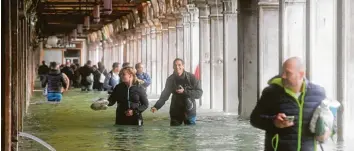  ??  ?? Touristen waten unter den Arkaden des überflutet­en Markusplat­zes in Venedig durchs Wasser.