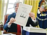  ?? Mike Theiler / Bloomberg ?? President Donald Trump holds the tax overhaul bill after signing it into law in the Oval Office last month.
