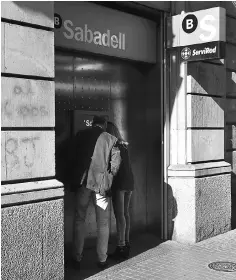  ?? — AFP photo ?? A couple withdraw cash from the ATM of a Sabadell Bank in Barcelona on October 5. Fitch warned it may downgrade the sovereign debt rating of Catalonia, a day after fellow ratings agency Standard & Poor’s issued a similar report as tensions with Madrid...
