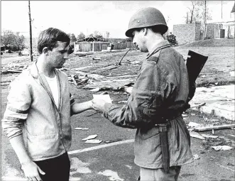  ??  ?? This photo by Photograph­er Bob Doty from the Dayton Daily News archives ran in the Journal Herald on May 13, 1969. According to the archives, Danny Critchlow is pictured being given a pass by Sgt. John Kniffin five days after a powerful tornado struck Kettering and Beavercree­k Twp.