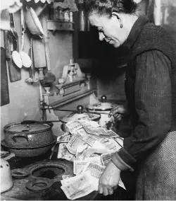  ??  ?? A German woman lights her stove with banknotes. In the early 1920s, marks lost value by the hour because of hyperinfla­tion