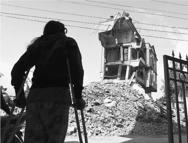  ?? ROBERTO SCHMIDT / AFP / Gett y Images ?? Nepalese resident Nomita Khadka, who twisted an ankle escaping the Nepal earthquake, looks at the remains of her home in Kathmandu on Friday.