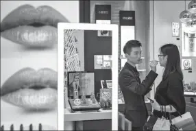  ?? QILAI SHEN / BLOOMBERG VIA GETTY IMAGES ?? A sales assistant helps a customer try out cosmetic products at a department store in Shanghai.