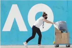  ?? — AFP ?? A worker wearing a face mask pushes a trolley in front of AO sign promoting Australian Open at the Melbourne Park in Melbourne.