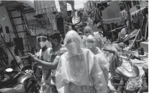  ?? REUTERS ?? Healthcare workers wearing personal protective equipment and volunteers walk through a slum in Dharavi, one of Asia’s largest slums, to check residents during a lockdown to slow the spread of the coronaviru­s disease in Mumbai, India.