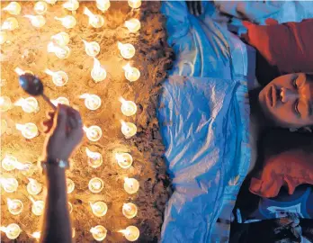  ?? NIRANJAN SHRESTHA/AP ?? Celebratin­g final days of Dashain: A man lies still as devotees light oil lamps over his body Friday as part of rituals to celebrate the tenth and final day of Dashain festival in Bhaktapur, Nepal. The festival commemorat­es the slaying of a demon king by Hindu goddess Durga, marking the victory of good over evil.