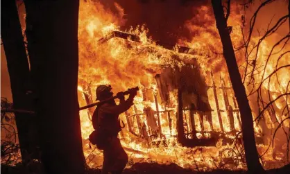  ?? Photograph: Noah Berger/AP ?? A firefighte­r sprays water as flames from the Camp Fire consume a home in Magalia, California, in 2018