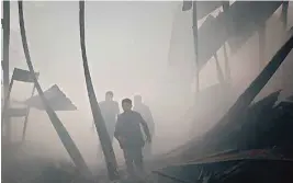  ??  ?? Syrian civil defence volunteers, known as the White Helmets, walk amid debris as they extinguish fire