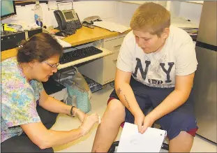  ??  ?? General Smallwood Middle School school nurse Sandra Geier, left, cleans a scar left behind after eighth grader Sean Heckman had stitches removed from his leg.