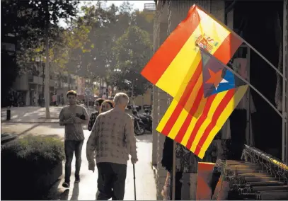  ?? Emilio Morenatti ?? The Associated Press People walk past the Spanish national flag and an estelada, or independen­ce flag, hanging up for sale in a shop in Barcelona.