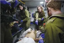  ?? (Baz Ratner/Reuters) ?? IDF SOLDIERS give initial medical treatment to wounded Syrians in a military ambulance on the Golan Heights last month.