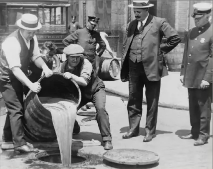  ?? Library of Congress ?? Prohibitio­n agents pour confiscate­d liquor into a sewer in New York City following a raid (circa 1921).