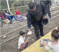  ??  ?? A Guatemalan police officer gives a migrant child some food as the migrants bound for the US-Mexico border wait on a bridge that stretches over the Suchiate River, connecting Guatemala and Mexico, yesterday.