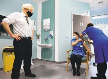  ?? STEFAN ROUSSEAU AP ?? British Prime Minister Boris Johnson watches as nurse Jennifer Dumasi receives the Oxford-AstraZenec­a vaccine during a visit to the Chase Farm Hospital in north London on Monday.