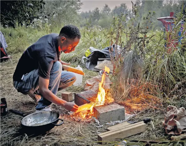  ??  ?? A migrant cooks on a small fire in a makeshift camp in wasteland on the outskirts of Calais. Recent evictions by French police at previously establishe­d camps have forced people to move to more remote areas. Left: migrants were spotted taking selfies as they waited to be rescued from an overloaded dinghy in the Channel