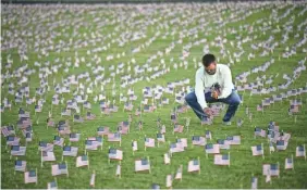  ?? JACK GRUBER/USA TODAY ?? At the National Mall on Monday, a volunteer helps place 200,000 American flags to memorializ­e U.S. deaths due to COVID-19.