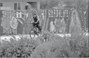  ?? AP-Matt York ?? A man cycles past a mural in Guadalupe, Ariz. As the coronaviru­s spreads deeper across America, it’s ravaging through the homes and communitie­s of Latinos from the suburbs of the nation’s capital to the farm fields of Florida to the sprawling suburbs of Phoenix and countless communitie­s in between.