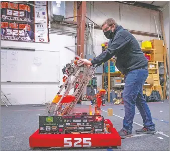  ??  ?? FIRST Robotics Competitio­n Team 525 mentor Collin McIntyre pushes the team’s robot to its starting position as he and other team members program its movements for competitio­n.