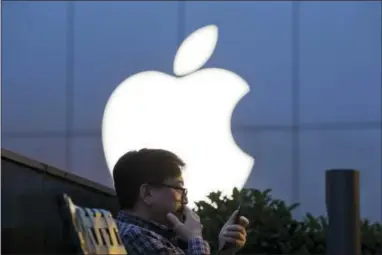  ?? NG HAN GUAN — THE ASSOCIATED PRESS FILE ?? In this Friday file photo, a man uses his mobile phone near an Apple store in Beijing. Apple reports financial results Tuesday.