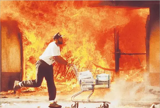  ?? Kirk McKoy Los Angeles Times ?? A MAN runs by buildings engulfed in flame after rioting erupted in L.A. for days in 1992 following the not-guilty verdict for officers charged in Rodney King’s beating.
