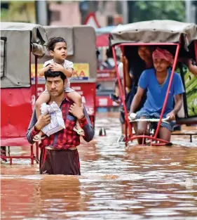  ?? AFP ?? A man carries his son as he walks through a flooded street after heavy rain in Guwahati on Thursday.