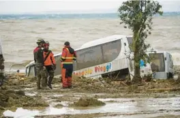  ?? SALVATORE LAPORTA/AP ?? Rescuers stand next to a bus resting in mud Saturday in Casamiccio­la, on the southern Italian island of Ischia near Naples, after heavy rainfall triggered landslides.