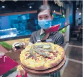  ?? SAKCHAI LALIT/AP ?? A staff member holds a pizza with a cannabis leaf last week at a restaurant in Bangkok, Thailand. The Pizza Company has been promoting its “Crazy Happy Pizza.”