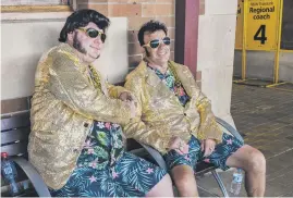  ?? ?? SALUTE TO THE KING. Two men dressed as Elvis Presley sit on a bench as people board a train to travel to the Elvis Festival.