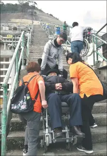  ?? KATHY ZHANG / CHINA DAILY ?? Mak, an operator (back), lifts a stair climber and helps Ng Lai-kuen (center), 90, to visit her husband’s grave on a hillside.