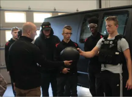  ?? KRISTI GARABRANDT — THE NEWS-HERALD ?? Eastlake detective Kris Korun shows Parker Jensen, a senior in the NCI Auto-body program, the tactical gear he would be wearing if called out as SWAT member in the van the students just painted for the Eastlake Police Police Department.