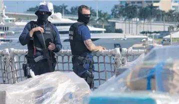  ?? JOE CAVARETTA/STAFF PHOTOGRAPH­ER ?? U.S. Coast Guard drug-interdicti­on personnel try to keep their identities concealed as they guard seized cocaine.