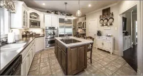  ??  ?? The kitchen features Corian countertop­s, ivory-wood cabinets, a central island and a walk-in pantry.