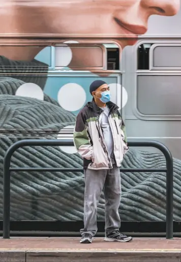  ?? Nick Otto / Special to The Chronicle ?? Bay Area residents, such as this masked passenger at a San Francisco bus stop, have taken steps to curtail the spread of the coronaviru­s.