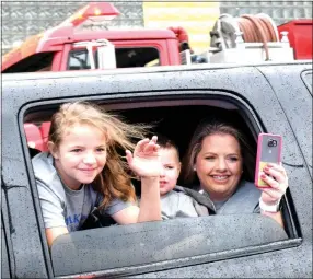  ?? Photo by Mike Eckels ?? From the rear window of their limousine, Remington Anderson (center) and one of his sisters wave to the many fire fighters lining Main St. in Decatur April 20 as their mother Tina takes a video of the event.