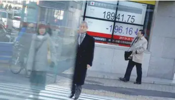  ?? — Reuters ?? People walk past an electronic board showing stock prices outside a brokerage at a business district in Tokyo, Japan.