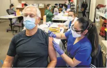  ?? Jessica Christian / The Chronicle ?? Christine Bernardo ( right) administer­s the first dose of the Moderna vaccine to Straty Righellis in Hayward.