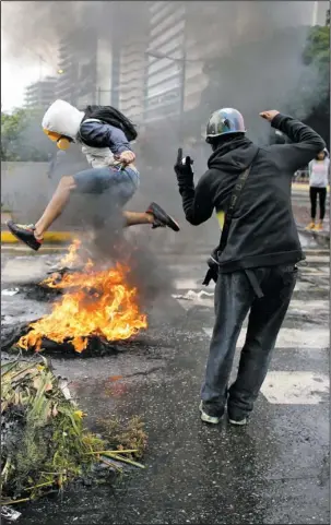  ?? The Associated Press ?? UNREST: A masked protester jumps over a burning barricade Wednesday in Caracas, Venezuela. The last 24 hours in Venezuela have been volatile, beginning with widespread looting in the coastal city of Maracay on Monday night and continued Tuesday with a...