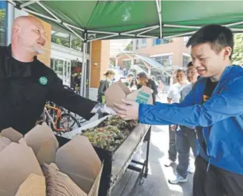  ?? Elaine Thompson, The Associated Press ?? Whole Foods Market Chef Hayden Smissen, left, hands a grilled chicken dish to Amazon worker Pandong Zhang, on lunch break from his office nearby, in Seattle. Amazon, already a powerhouse in books, shoes, streaming video, electronic­s and just about...