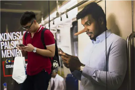  ??  ?? Make sure it’s real: A commuter (red T-shirt) reading news from his mobile phone next to an advertisem­ent discouragi­ng the disseminat­ion of fake news at a train station in Kuala Lumpur.