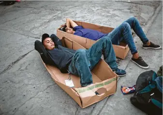  ?? Rodrigo Abd / Associated Press ?? Hondurans Roney Santos, left, and Benjamin Perez, use cardboard to rest on the pavement before eating dinner in downtown Mexicali, Mexico. Tensions have built as nearly 3,000 migrants from a caravan poured into Tijuana in recent days, hoping to seek asylum in the United States.