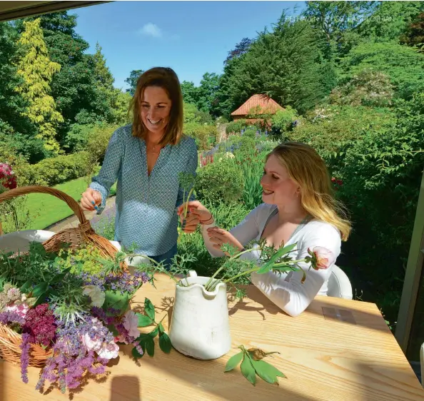  ??  ?? Top left: An outdoor table seen through a curtain of red Valerian. Above: Roz (left) arranging flowers with her daughter Hannah.
Below left: A quiet woodland corner with chairs and small sculpture.