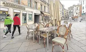  ??  ?? POCO MOVIMIENTO. Dos ciudadanos pasan por la terraza de un café en Venecia, que está cerrado.