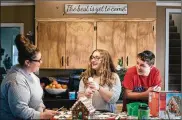  ??  ?? Hannah Thurman, 17, and James Thurman, 15, decorate a gingerbrea­d house with Christina Burns, the aunt with whom they have lived for years, in Portsmouth.