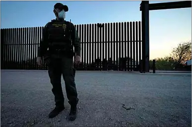  ?? JULIO CORTEZ / AP ?? A U.S. Customs and Border Protection agent looks on near a gate on the U.S.-Mexico border wall as agents take migrants into custody Sunday in Abram-Perezville, Texas.