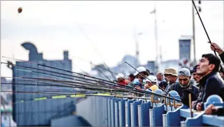  ?? OZAN KOSE/AFP ?? People fish from the Galata Bridge in Karakoy district in Istanbul on October 23, as a new mosque is seen in the background.