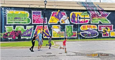  ?? [CHRIS LANDSBERGE­R/ THE OKLAHOMAN] ?? Anthony Drake Jr., of Oklahoma City, walks with his children, from left, Legacy, Genesis and Anthony, past the Black Wall Street mural in Tulsa's Greenwood Distric.