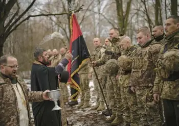  ?? VADIM GHIRDA/AP ?? A priest blesses soldiers with holy water Saturday in Kharkiv, Ukraine, during a ceremony where they were honored for their bravery and accomplish­ments in the war against Russia, now more than a year old.